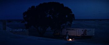 Movie still from “Road Games” (1981), directed by Richard Franklin – A person standing next to a fire in the dark; Extreme Wide shot, Low angle