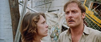 Movie still from “Road Games” (1981), directed by Richard Franklin – A man and a woman standing next to each other in front of barbed wire; Close Up shot, Low angle