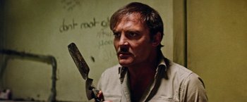 Movie still from “Road Games” (1981), directed by Richard Franklin – A man holding a knife in a room with writing on the wall behind him; Close Up shot, Low angle