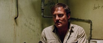 Movie still from “Road Games” (1981), directed by Richard Franklin – A man with a mustache sitting in a room; Close Up shot, Low angle