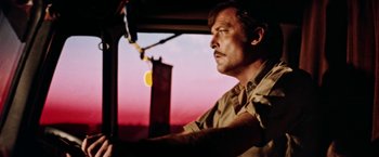 Movie still from “Road Games” (1981), directed by Richard Franklin – A man sitting in the driver's seat of a vehicle; Close Up shot, Low angle
