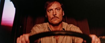 Movie still from “Road Games” (1981), directed by Richard Franklin – A person with a mustache driving a car; Close Up shot, Low angle