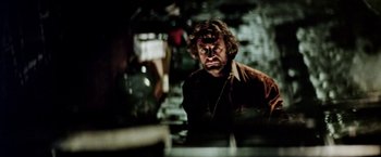 Movie still from “Road Games” (1981), directed by Richard Franklin – A man in a brown jacket is looking at the camera; Medium shot, Low angle