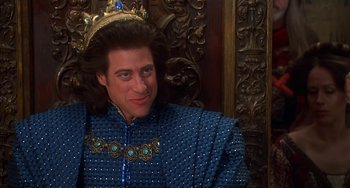Movie still from “Robin Hood: Men in Tights” (1993), directed by Mel Brooks – A man wearing a blue robe and a gold crown; Close Up shot, Over the shoulder angle