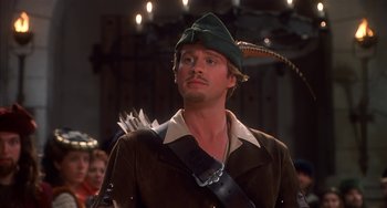 Movie still from “Robin Hood: Men in Tights” (1993), directed by Mel Brooks – A person wearing a hat and holding a bow and arrow; Close Up shot, Over the shoulder angle