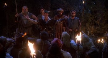 Movie still from “Robin Hood: Men in Tights” (1993), directed by Mel Brooks – A group of people standing in front of a fire pit; Medium shot, Over the shoulder angle