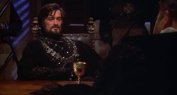 Movie still from “Robin Hood: Men in Tights” (1993), directed by Mel Brooks – A man sitting at a table with a glass of wine; Medium shot, Over the shoulder angle