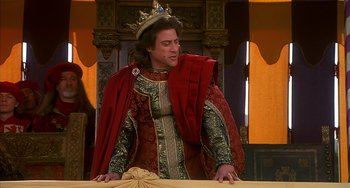 Movie still from “Robin Hood: Men in Tights” (1993), directed by Mel Brooks – A man wearing a crown standing in front of a table; Medium shot, Over the shoulder angle