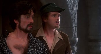 Movie still from “Robin Hood: Men in Tights” (1993), directed by Mel Brooks – A man wearing a green hat standing next to another man wearing a brown jacket; Close Up shot, Over the shoulder angle