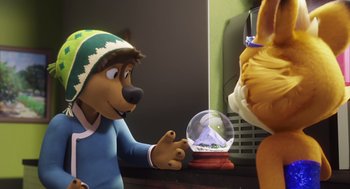 Movie still from “Rock Dog 2: Rock Around the Park” (2021), directed by Mark Baldo – A person holding a snow globe in front of a bear; Medium shot, Over the shoulder angle