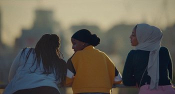 Movie still from “Rocks” (2019), directed by Sarah Gavron – A group of young women standing next to each other; Medium shot, Over the shoulder angle