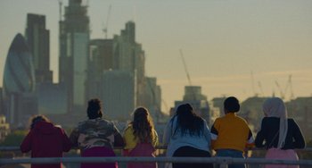 Movie still from “Rocks” (2019), directed by Sarah Gavron – A group of people sitting on top of a bench; Extreme Wide shot, Over the shoulder angle