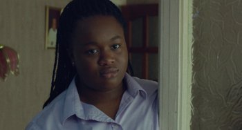 Movie still from “Rocks” (2019), directed by Sarah Gavron – A young woman in a purple shirt looking out a window; Close Up shot, Over the shoulder angle