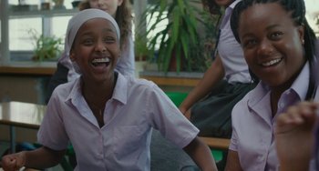 Movie still from “Rocks” (2019), directed by Sarah Gavron – A group of young people sitting on a bench laughing; Medium shot, Over the shoulder angle