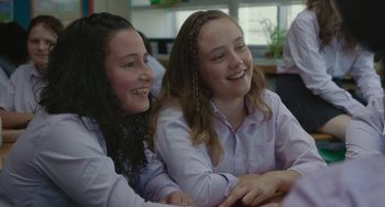 Movie still from “Rocks” (2019), directed by Sarah Gavron – Two young women sitting next to each other in front of a window; Close Up shot, Over the shoulder angle