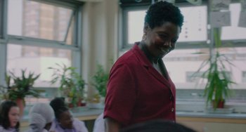 Movie still from “Rocks” (2019), directed by Sarah Gavron – A woman in a red shirt is smiling at the camera; Medium shot, Over the shoulder angle