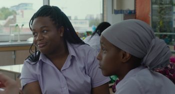 Movie still from “Rocks” (2019), directed by Sarah Gavron – Two young women sitting next to each other in front of a window; Close Up shot, Over the shoulder angle
