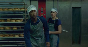 Movie still from “Rocks” (2019), directed by Sarah Gavron – A man and a woman wearing aprons in a kitchen; Medium shot, Low angle