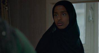 Movie still from “Rocks” (2019), directed by Sarah Gavron – A young woman wearing a black headscarf looking at the camera; Close Up shot, Over the shoulder angle
