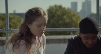 Movie still from “Rocks” (2019), directed by Sarah Gavron – A young girl sitting next to another young person; Close Up shot, Over the shoulder angle