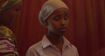 Movie still from “Rocks” (2019), directed by Sarah Gavron – A woman wearing a head scarf and a button down shirt; Close Up shot, Over the shoulder angle