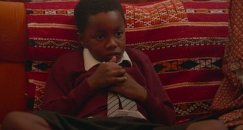 Movie still from “Rocks” (2019), directed by Sarah Gavron – A young boy sitting on top of a red couch; Close Up shot, High angle
