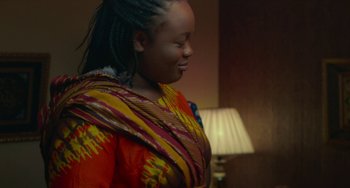 Movie still from “Rocks” (2019), directed by Sarah Gavron – A woman in a brightly colored dress is smiling; Medium shot, Over the shoulder angle