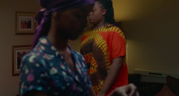 Movie still from “Rocks” (2019), directed by Sarah Gavron – Two people standing in a room with one of them wearing a tye - dye shirt; Medium shot, Over the shoulder angle
