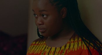 Movie still from “Rocks” (2019), directed by Sarah Gavron – A woman with long braids wearing an orange and yellow shirt; Close Up shot, Over the shoulder angle
