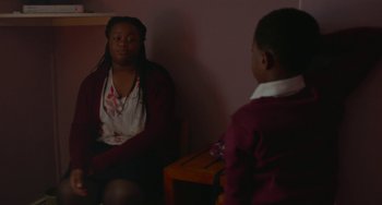 Movie still from “Rocks” (2019), directed by Sarah Gavron – A woman sitting in front of a boy in a room; Medium shot, Over the shoulder angle