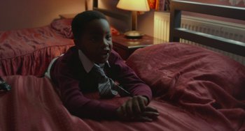 Movie still from “Rocks” (2019), directed by Sarah Gavron – A young boy laying on a bed in a room; Medium shot, High angle