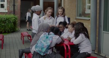 Movie still from “Rocks” (2019), directed by Sarah Gavron – A group of young people sitting around a red table; Wide shot, High angle