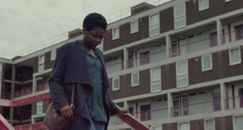 Movie still from “Rocks” (2019), directed by Sarah Gavron – A woman walking in front of an apartment building; Medium shot, Low angle