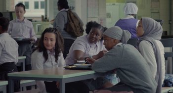 Movie still from “Rocks” (2019), directed by Sarah Gavron – A group of people sitting around a table; Medium shot, Over the shoulder angle