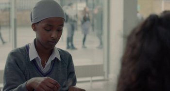 Movie still from “Rocks” (2019), directed by Sarah Gavron – A young person sitting in front of a window; Close Up shot, Over the shoulder angle