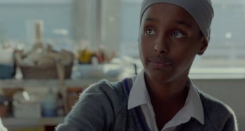 Movie still from “Rocks” (2019), directed by Sarah Gavron – A woman with a head scarf looking at the camera; Close Up shot, Over the shoulder angle