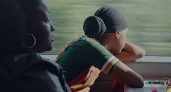 Movie still from “Rocks” (2019), directed by Sarah Gavron – Two people sitting next to each other on a bench; Medium shot, Over the shoulder angle