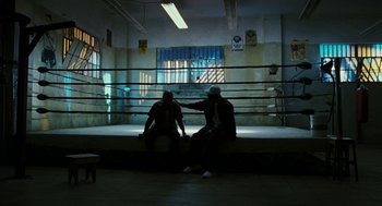 Movie still from “Rocky Balboa” (2006), directed by Sylvester Stallone – Two men sitting in a boxing ring in front of a cage; Wide shot, High angle