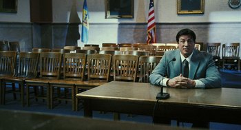 Movie still from “Rocky Balboa” (2006), directed by Sylvester Stallone – A man sitting at a table in front of microphones; Wide shot, High angle