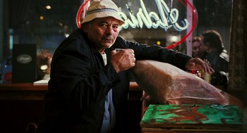 Movie still from “Rocky Balboa” (2006), directed by Sylvester Stallone – An older man sitting in front of a neon sign; Medium shot, Low angle