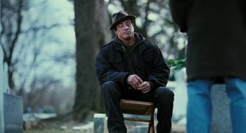 Movie still from “Rocky Balboa” (2006), directed by Sylvester Stallone – A man sitting on top of a chair in a forest; Wide shot, Over the shoulder angle