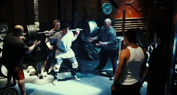 Movie still from “Rocky Balboa” (2006), directed by Sylvester Stallone – A group of people in a gym lifting barbells; Wide shot, Over the shoulder angle