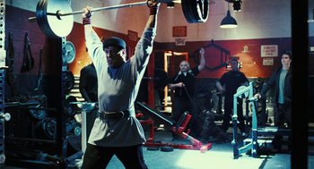 Movie still from “Rocky Balboa” (2006), directed by Sylvester Stallone – A man lifting a barbell in a gym; Medium shot, Over the shoulder angle