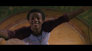 Movie still from “Roll Bounce” (2005), directed by Malcolm D. Lee – A young man is smiling for the camera; Medium shot, Low angle