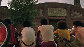 Movie still from “Roll Bounce” (2005), directed by Malcolm D. Lee – A group of young men sitting in front of a building; Wide shot, Low angle