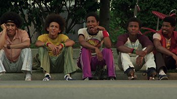 Movie still from “Roll Bounce” (2005), directed by Malcolm D. Lee – A group of young men sitting next to each other on the ground; Medium shot, Low angle