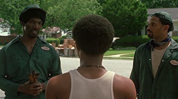 Movie still from “Roll Bounce” (2005), directed by Malcolm D. Lee – A man standing next to two other men in front of a house; Medium shot, Over the shoulder angle