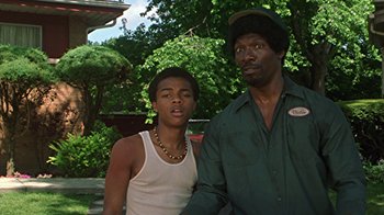 Movie still from “Roll Bounce” (2005), directed by Malcolm D. Lee – A man standing next to a young boy in front of a tree; Medium shot, Low angle