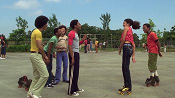 Movie still from “Roll Bounce” (2005), directed by Malcolm D. Lee – A group of young people standing around a girl on a skateboard; Wide shot, Low angle