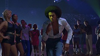 Movie still from “Roll Bounce” (2005), directed by Malcolm D. Lee – A man in a white shirt and a green afro is in the middle of a crowd of people; Medium shot, Low angle